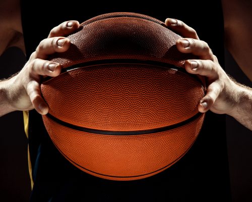 The silhouette view of a basketball player holding basket ball on black background. The hands and ball close up